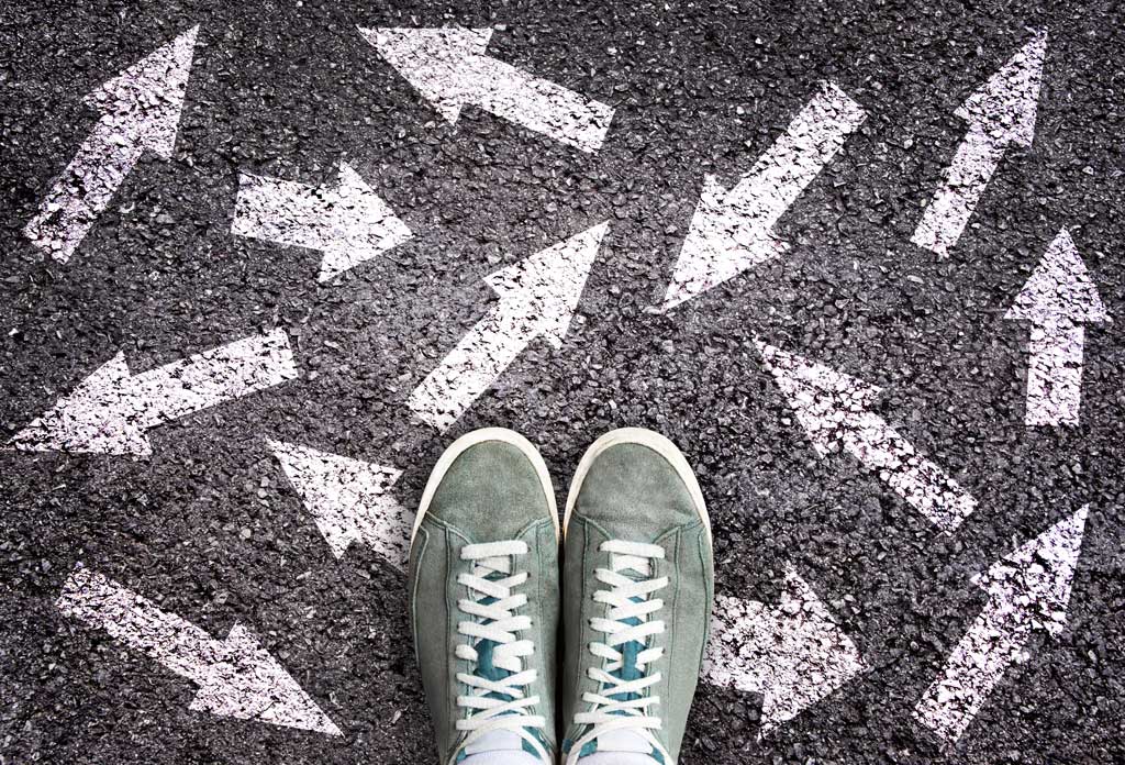 A pair of green sneakers on asphalt surrounded by painted white arrows pointing in all directions