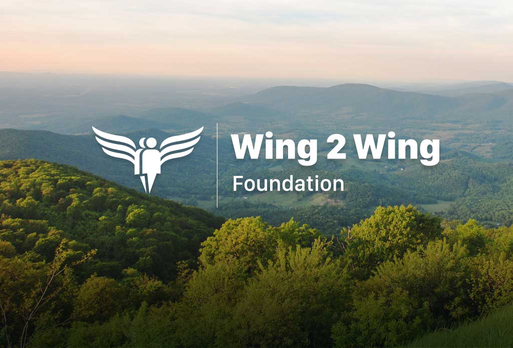 White "Wing 2 Wing Foundation" Text over a picture of mountains
