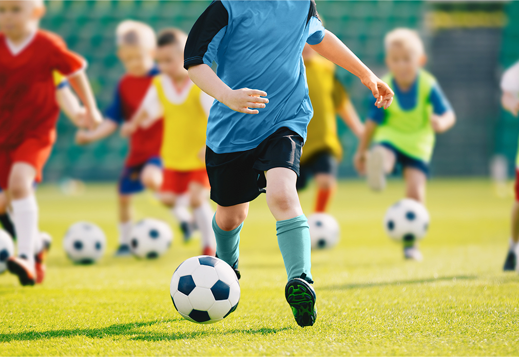 Child kicking a soccer ball with other children doing the same in the background