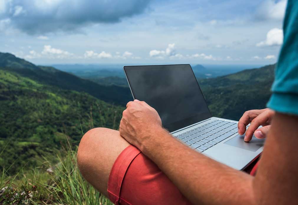 Person holding a laptop with mountains in the background