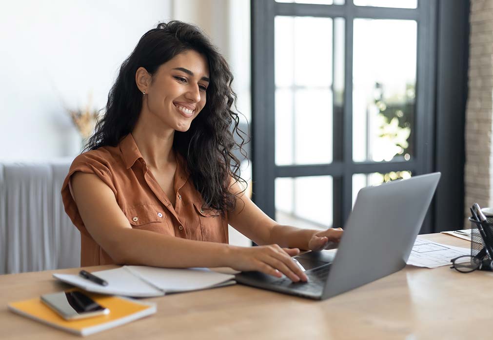 Woman smiling and looking at laptop as she is typing