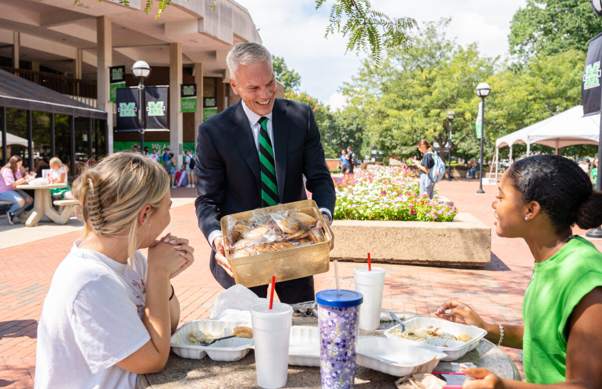 Marshall University President Brad D. Smith giving out cookies to students sitting down
