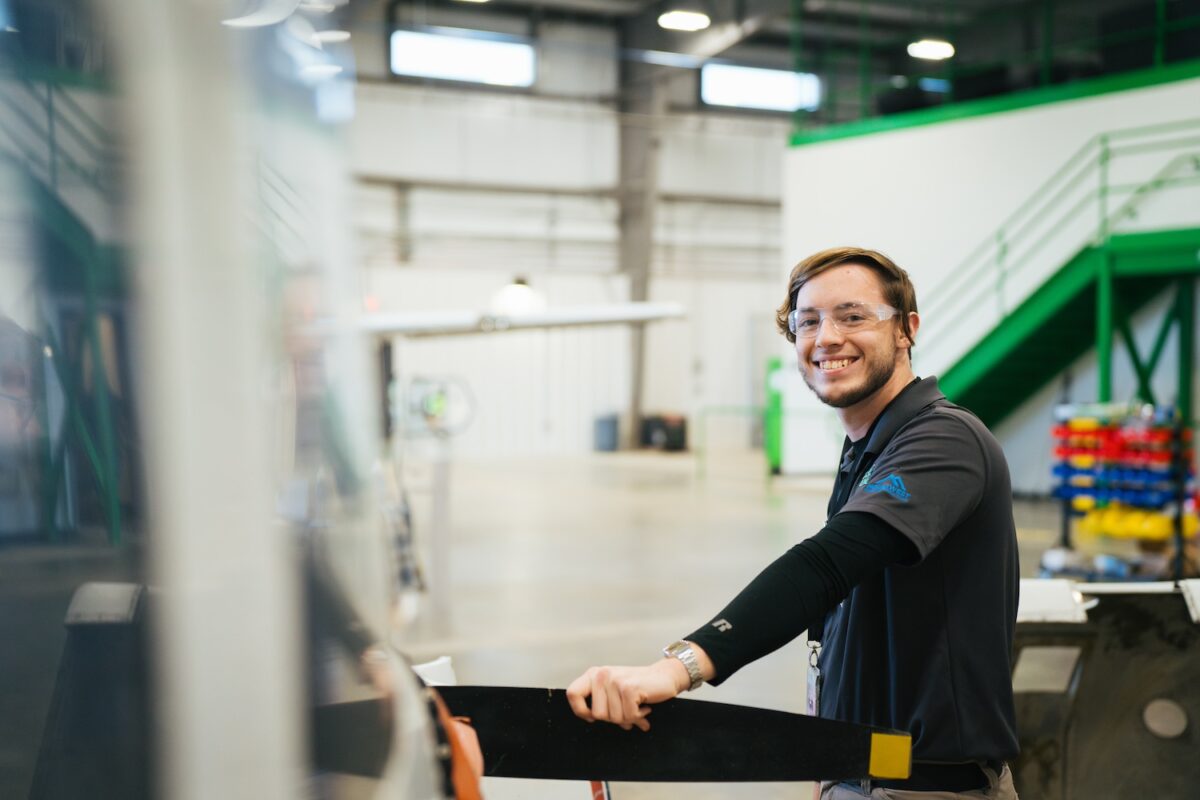 A Marshall University student smiles at the camera holding on to the propellor of a plane.