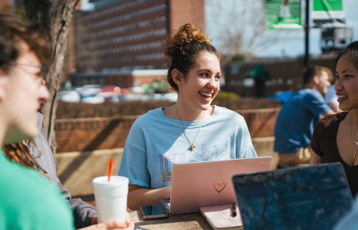 A Marshall University student laughs with her friends in front of her laptop on campus.