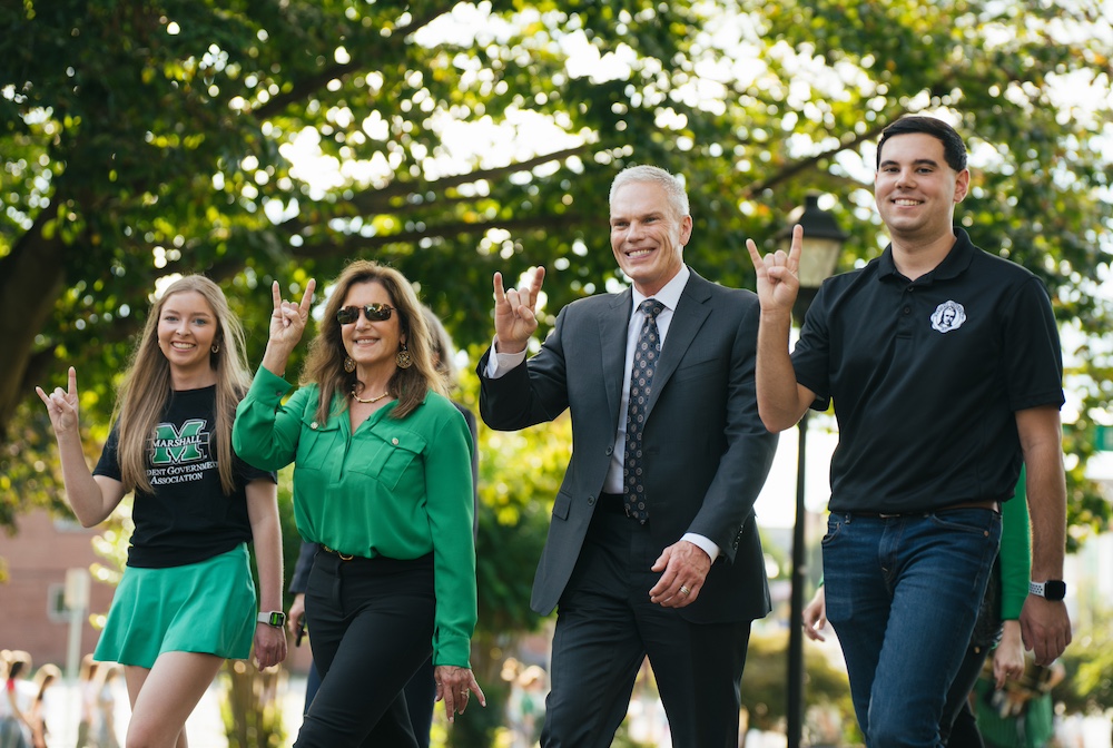 Brad and Alys Smith throw The Herd horns as they walk alongside students at the Marshall University homecoming Unity Walk.