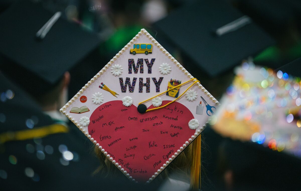 Close-up shot of decorated graduation cap with the words “My Why” and a list of people’s signatures.