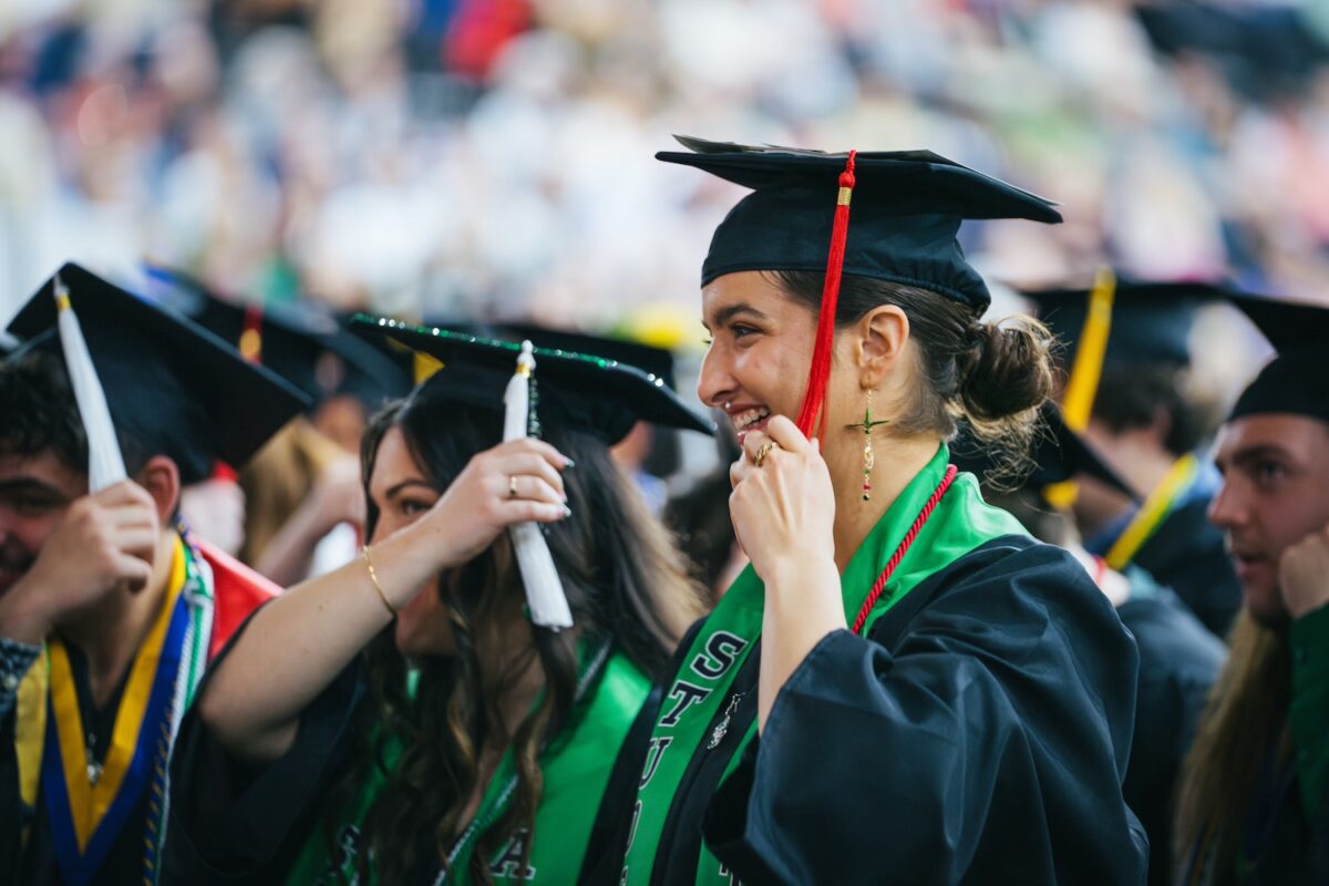 Marshall University graduates smiling at commencement ceremony about to move their tassels to the other side of their caps.