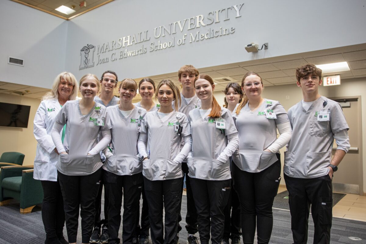 Med EX 2025 students smile for a photo in the foyer of the Joan C. Edwards School of Medicine.