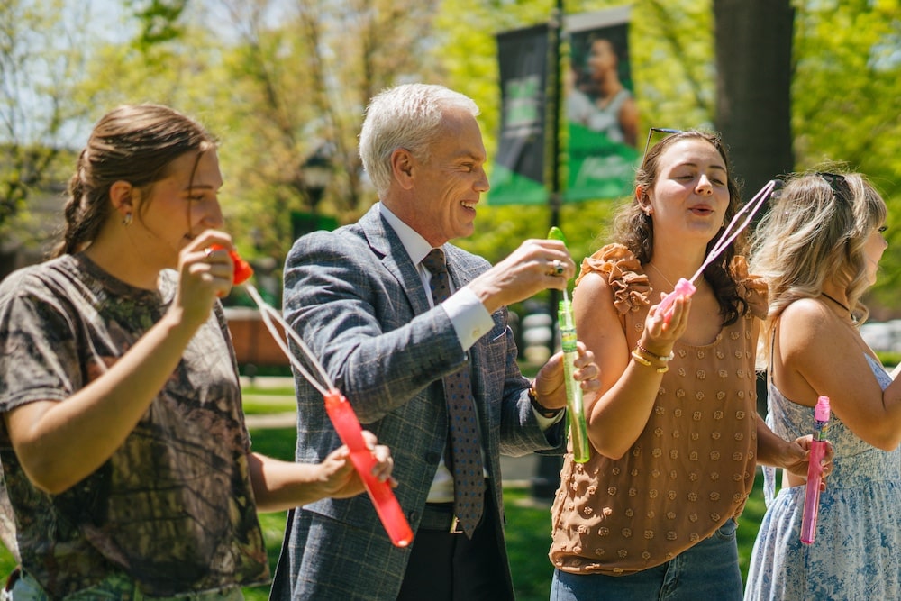 Brad D. Smith blows bubbles with students on the Marshall University campus.