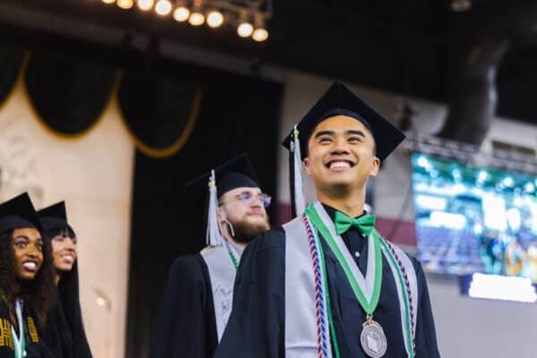 A Marshall University graduate stands proudly on the stage smiling.