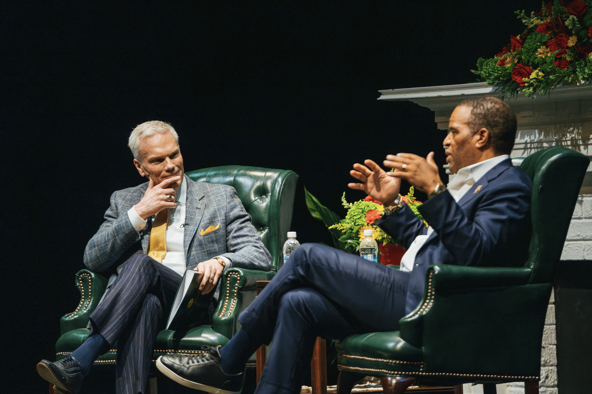 Brad D. Smith in a gray suit and yellow tie, sitting across the stage from John Hope Bryant in a navy suit